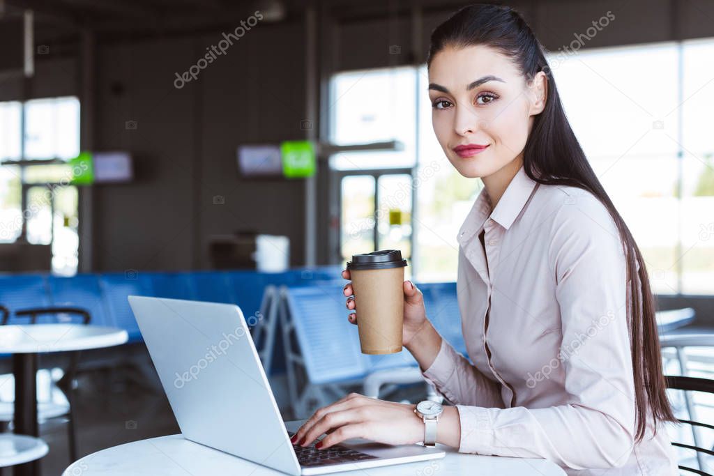 young businesswoman drinking coffee and using laptop at airport