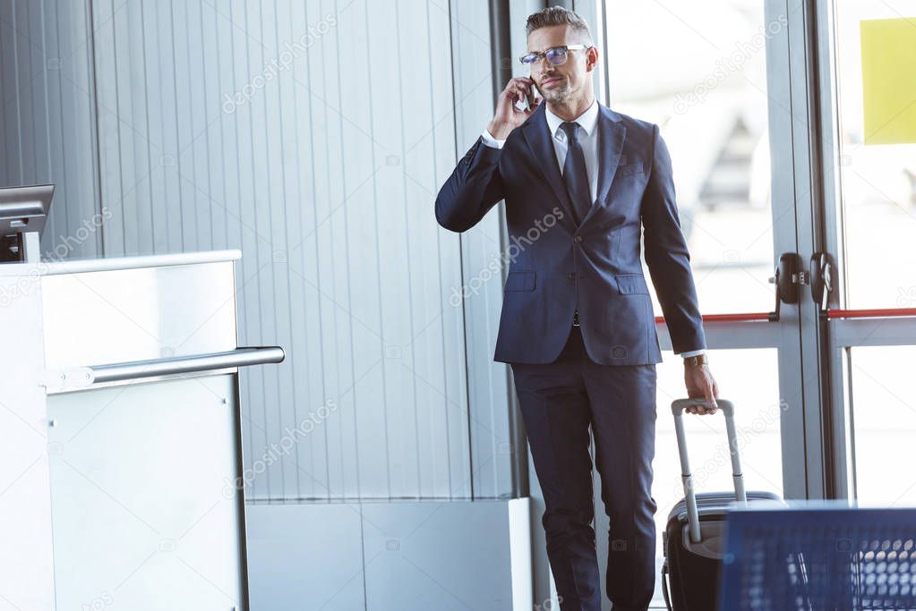 adult businessman in glasses with smartphone walking at airport
