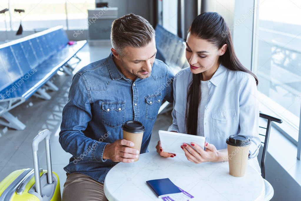 adult couple drinking coffee and using digital tablet in airport