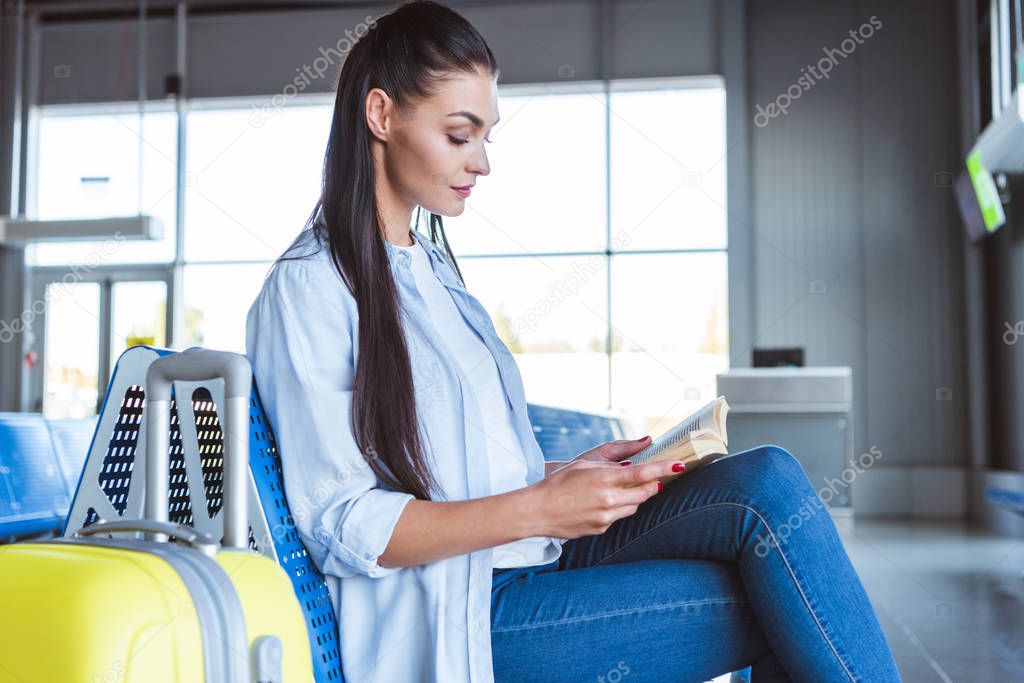 Beautiful woman with yellow luggage reading a book in the airport