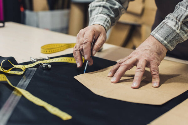 cropped image of male leather handbag craftsman working at studio