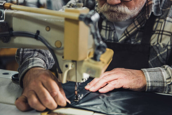 partial view of male tailor working on sewing machine at studio