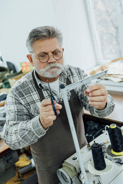 высокий угол обзора зрелого мужского портного в фартуках на швейной машинке в мастерской
