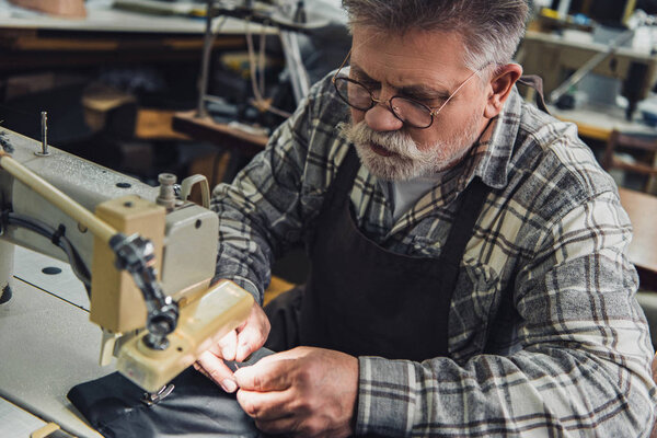 high angle view of male handbag craftsman working on sewing machine at studio