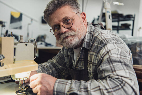 portrait of happy male handbag craftsman working on sewing machine at studio