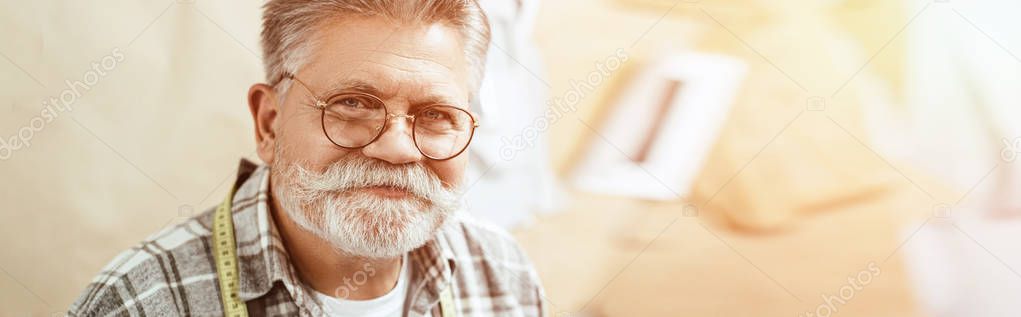 portrait of happy mature craftsman in eyeglasses looking at camera in studio