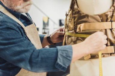 cropped image of mature male tailor making measurements on military vest at workshop clipart