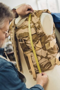 partial view of mature male tailor making measurements on military vest at workshop clipart