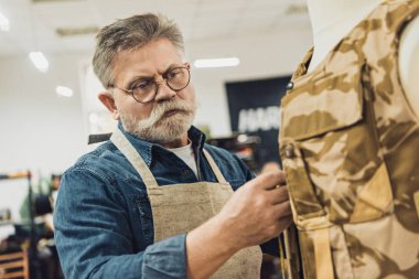 focused middle aged male tailor making measurements on military vest at workshop clipart