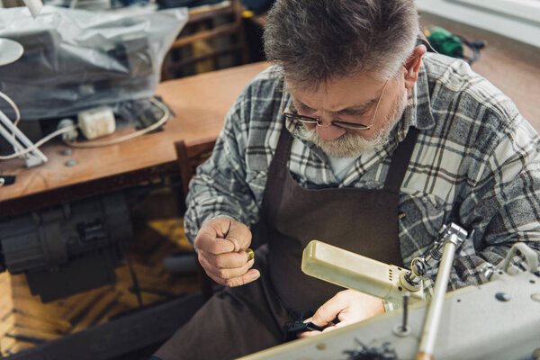 high angle view of middle aged male tailor in eyeglasses and apron sewing at workshop