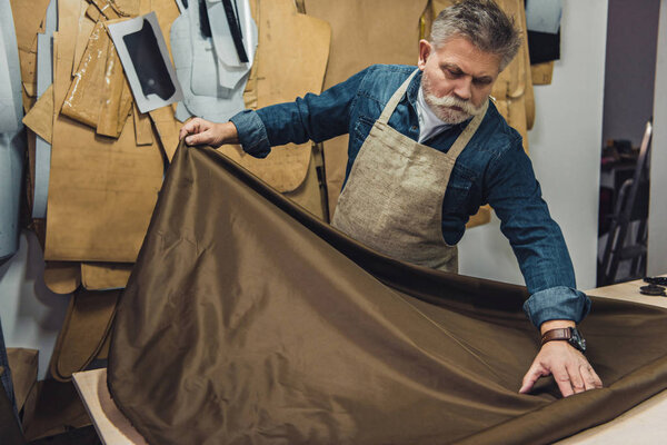 middle aged male handbag craftsman putting fabric on working table at studio