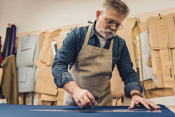 low angle view of male middle aged craftsman in apron making measurements on fabric at workshop