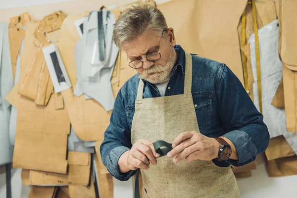 中間の老化させた男性ハンドバッグ職人エプロン 眼鏡工房布で作業を集中してください — ストック写真