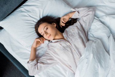 top view of beautiful brunette woman in pajamas sleeping on bed in the morning clipart