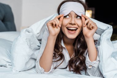beautiful excited girl in sleeping eye mask lying in bed clipart