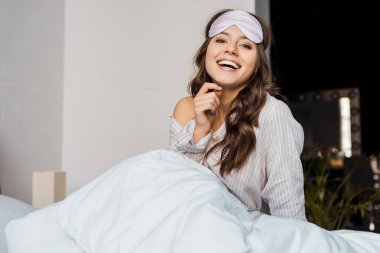 attractive laughing girl in sleeping eye mask lying in bed clipart