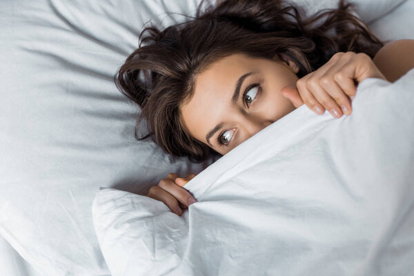 красивая девушка прячется под белым одеялом на кровати
