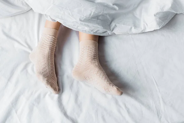 Teilaufnahme Von Mädchen Socken Die Unter Weißer Decke Bett Liegen — Stockfoto