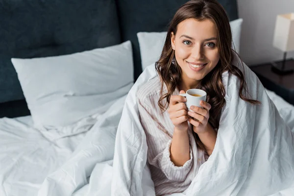 朝はベッドに座ってコーヒーのカップと笑顔の女の子 — ストック写真