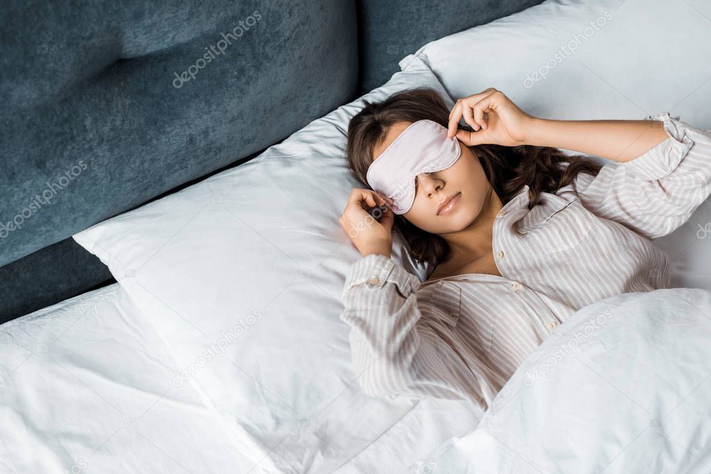 young woman in sleeping eye mask waking up in bed in the morning