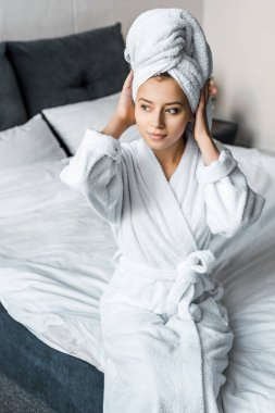 beautiful girl in white bathrobe wearing towel on head while sitting on bed clipart