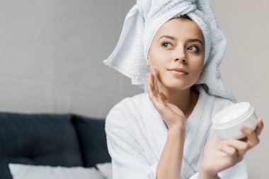 beautiful girl with towel on head applying cosmetic cream on face clipart