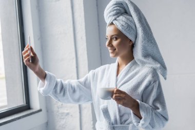 selfie fincan kahve ile sabah Smartphone'da alarak bornoz gülümseyen kız