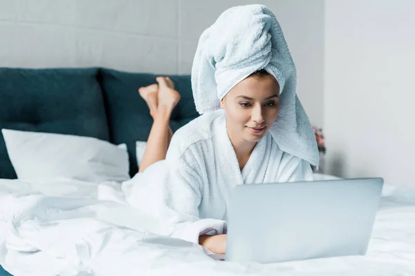 朝のベッドの上に横たわっている間ノート パソコンを使用してのバスローブの美しい若い女性 — ストック写真