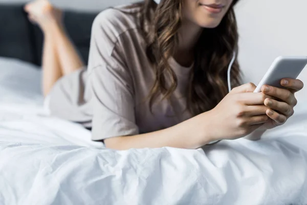 Kadın Yatakta Yatarken Akıllı Telefon Kulaklık Ile Müzik Dinleme Kırpılmış — Stok fotoğraf