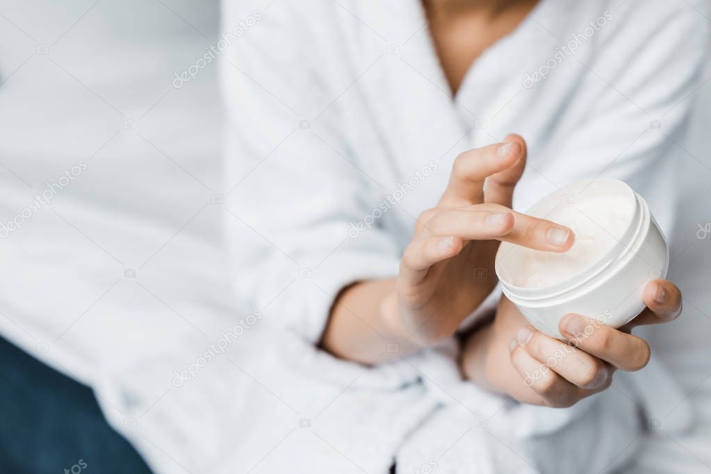 partial view of girl with cosmetic cream in plastic container