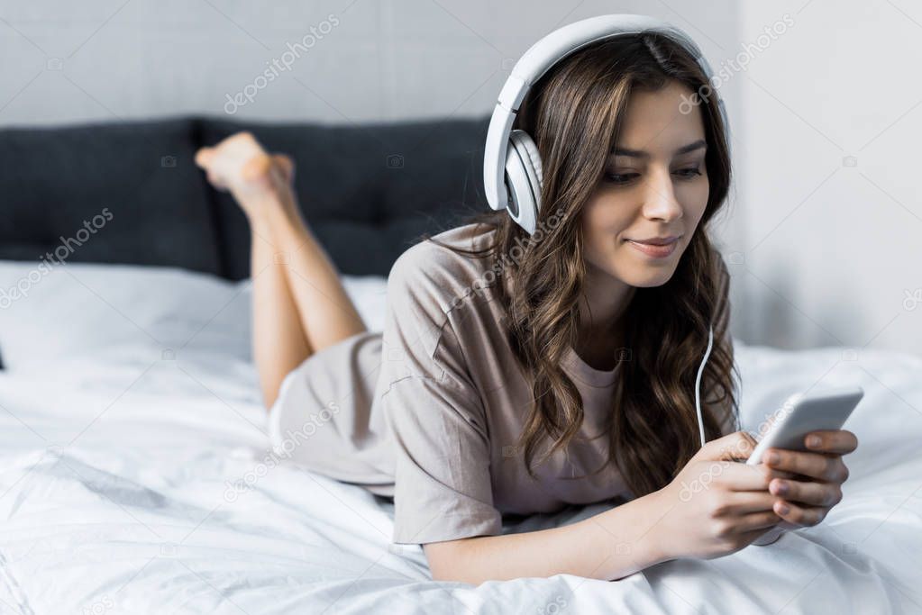 beautiful brunette girl listening music with headphones and smartphone while lying on bed