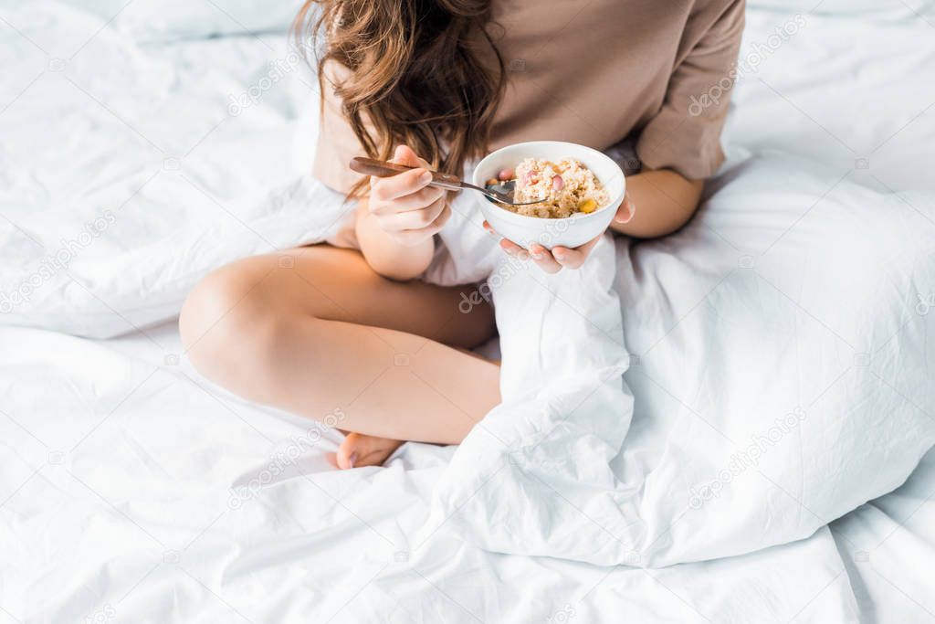 cropped view of girl having oatmeal for breakfast in bed