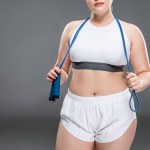 Schnappschuss einer jungen übergroßen Frau in Sportbekleidung mit Springseil auf grau