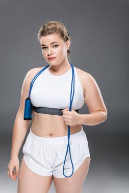 çekici genç büyük boy kadın spor giyim holding atlama ipi ve kameraya gri arıyor