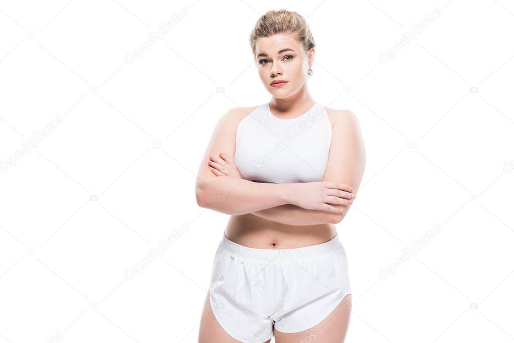 young oversize woman in sportswear standing with crossed arms and looking at camera isolated on white 