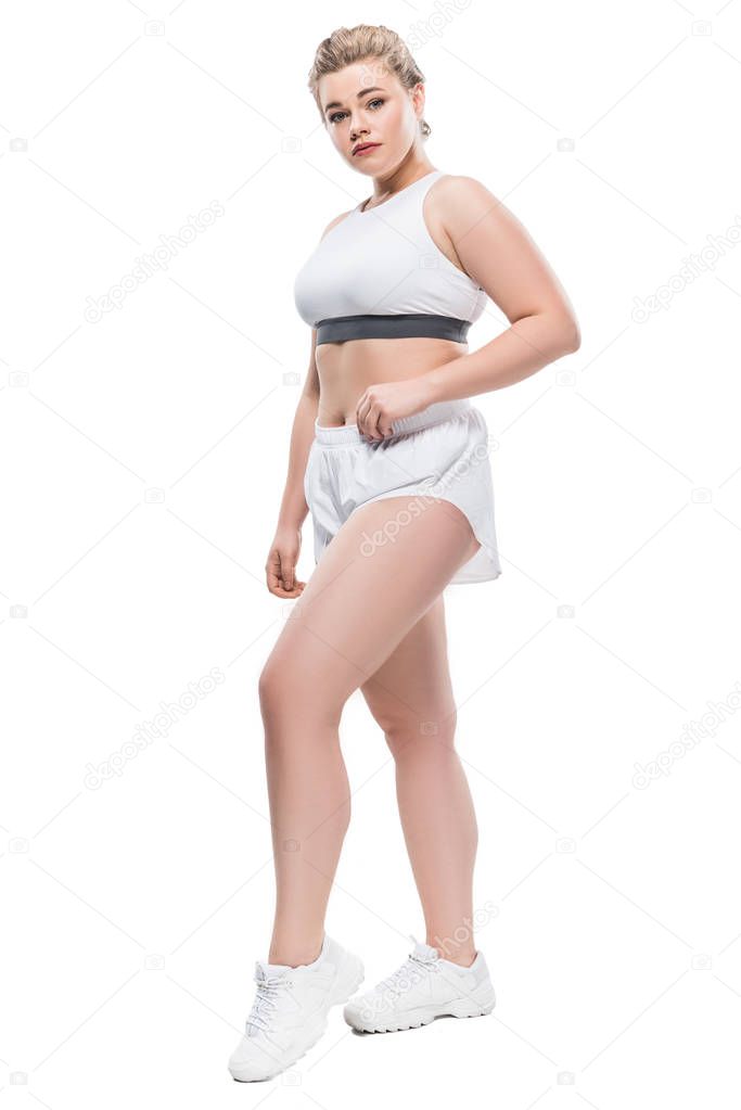 full length view of attractive oversize girl in sportswear looking at camera isolated on white