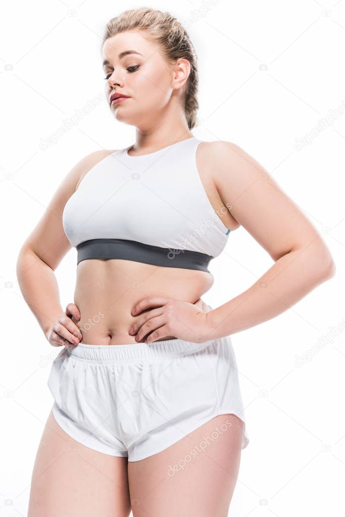 low angle view of young overweight woman in sportswear standing with hands on waist isolated on white 