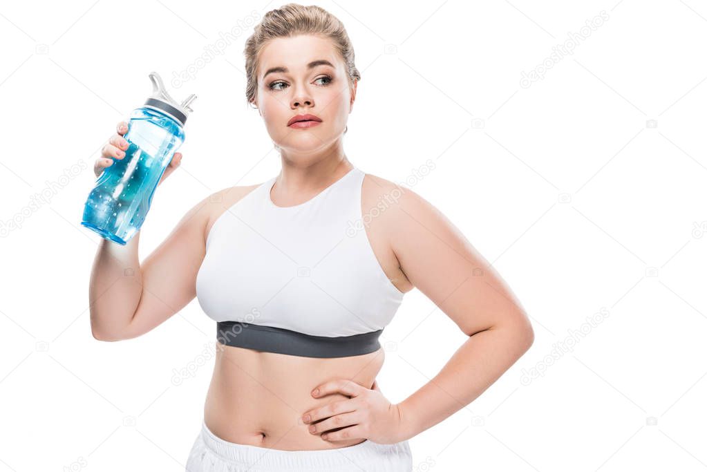 size plus woman in sportswear holding bottle of water and looking away isolated on white