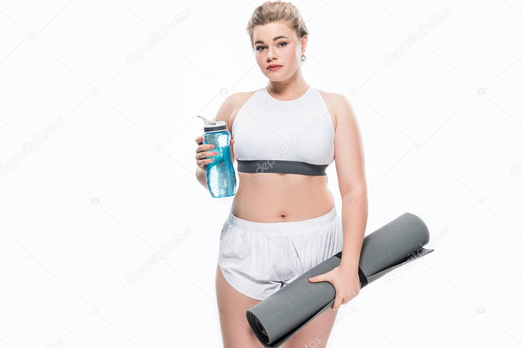attractive overweight girl in sportswear holding bottle of water and yoga mat isolated on white  