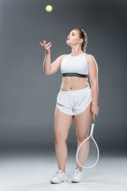 Genç kilolu kadın tenis raketi tutarak ve gri topu atma