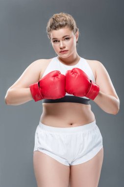 güzel genç kilolu kadın spor giyim ve boks eldivenleri gri izole kamera bakıyor