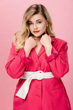 elegant young woman in pink trench coat looking at camera isolated on pink  clipart