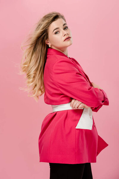 side view of beautiful stylish oversize woman standing with crossed arms and looking at camera isolated on pink 