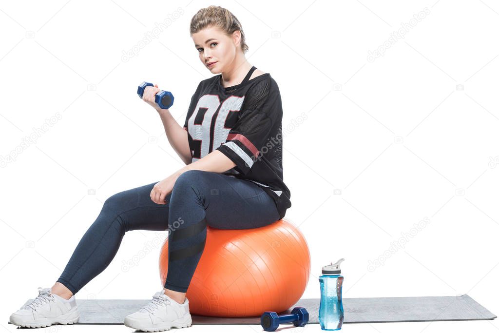 young overweight woman sitting on fit ball and exercising with dumbbell isolated on white 