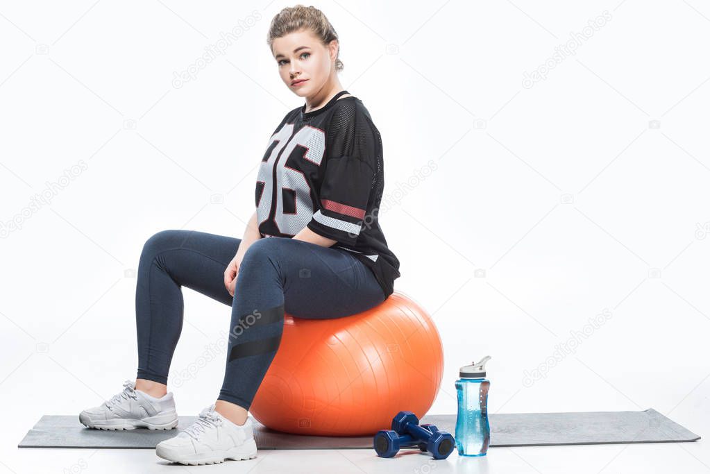 beautiful young overweight woman sitting on fit ball and looking at camera isolated on white  