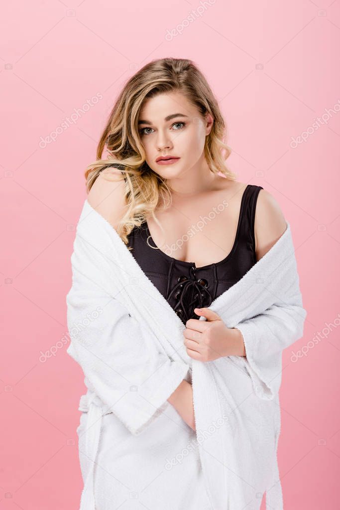 beautiful oversize woman in bathrobe and swimsuit looking at camera isolated on pink 