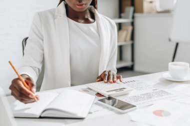 Not defterinde yazılı ve ofis masa başında çalışan beyaz formal giyim Afro-Amerikan yetişkin işkadını görünümünü kırpılmış