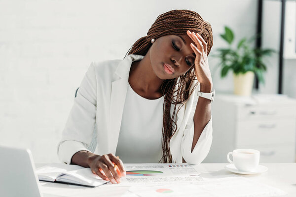 tired african american adult businesswoman sitting at desk and working on project in office