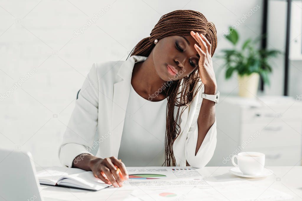 tired african american adult businesswoman sitting at desk and working on project in office