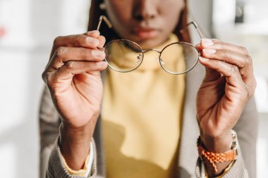 cropped view of african american adult businesswoman in formal wear putting on glasses clipart